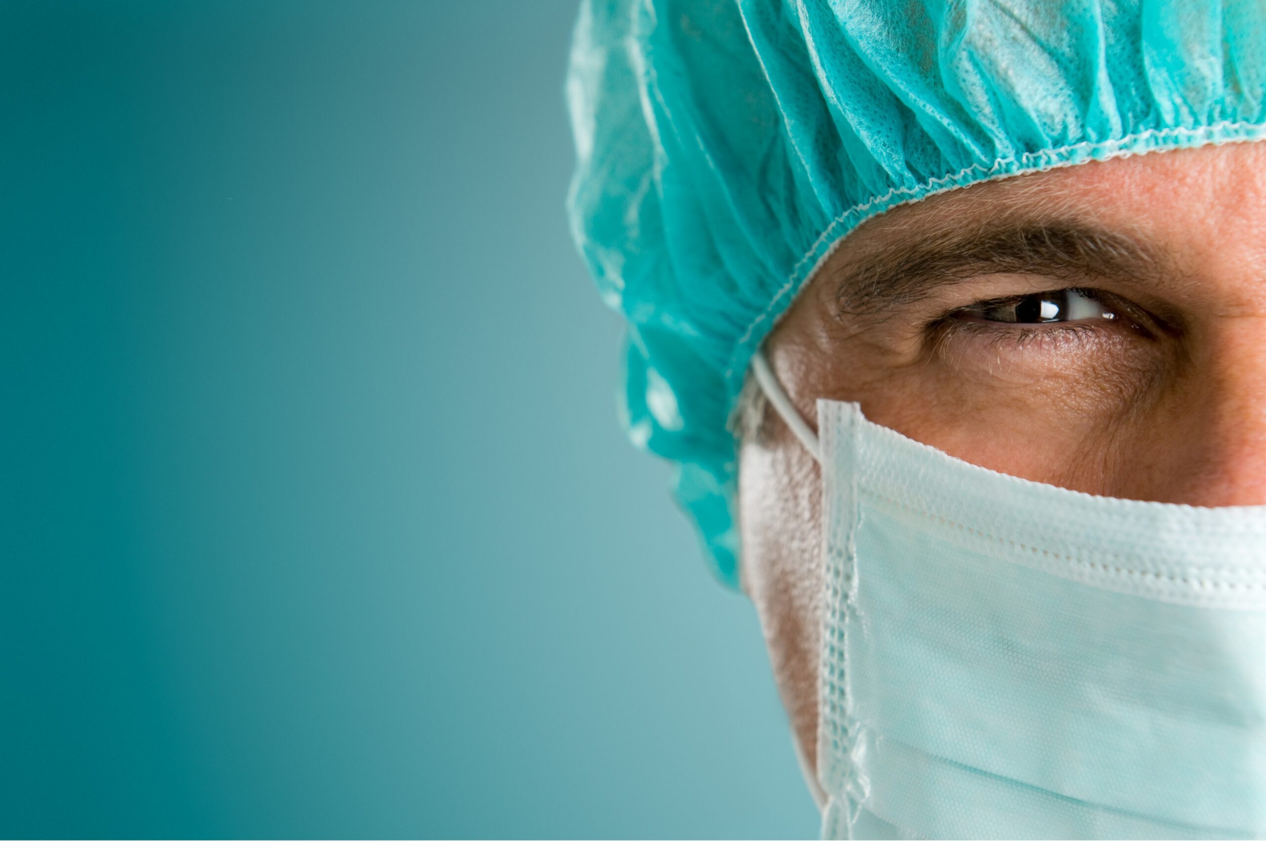 Close view of a vascular surgeon smiling for the camera wearing a green cap and mask.